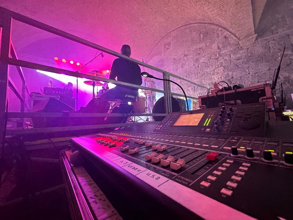 Mixer Yamaha LS9 in regia e palco illuminato di magenta sotto una volta in pietra