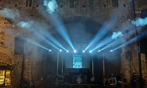 Fasci di luce bianca resi solidi dal fumo sopra il palco allestito sotto un arco in pietra
