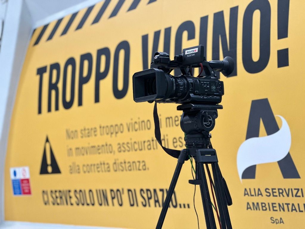 Telecamera professionale su cavalletto pronta alla ripresa davanti al fondale giallo di un evento aziendale