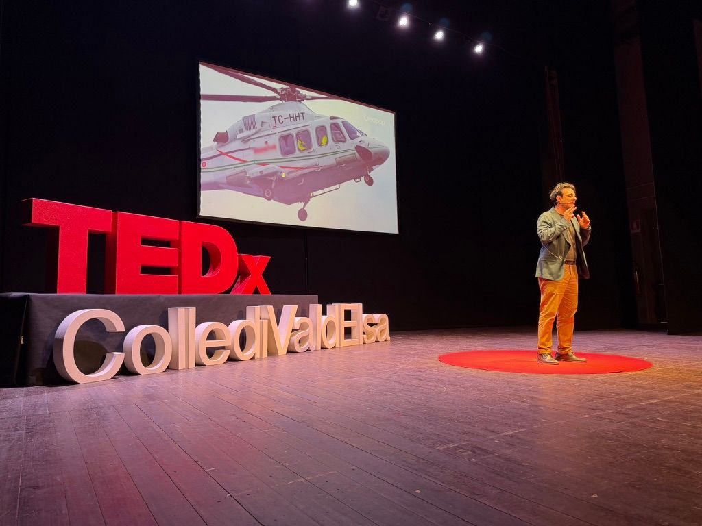 Palco TEDx con lettere tridimensionali, schermo di proiezione e relatore