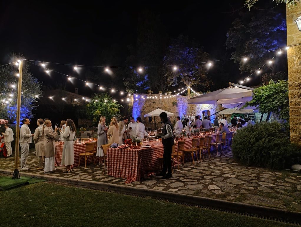 Cena di matrimonio in giardino sotto catenarie su pali, muro in pietra illuminato di blu