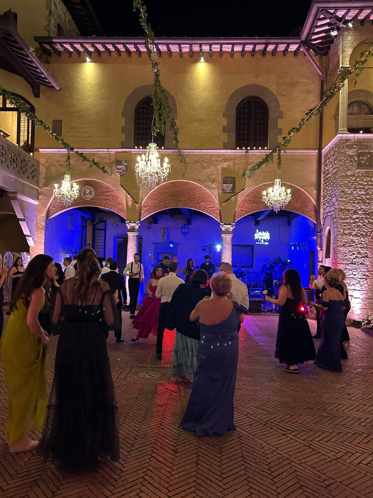 Pista da ballo piena di invitati nel cortile storico, band sotto il portico illuminato di blu