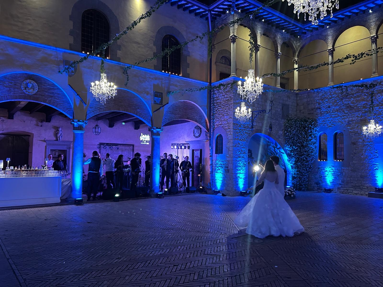 Sposi al primo ballo mentre la band dal vivo suona nel cortile porticato, fra lampadari di cristallo e luci blu
