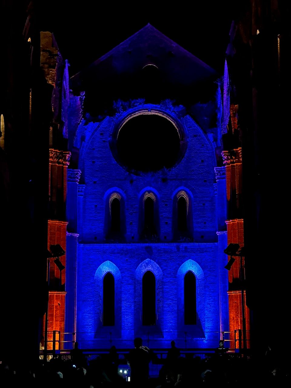 Transept of San Galgano abbey lit in blue and orange during an evening concert