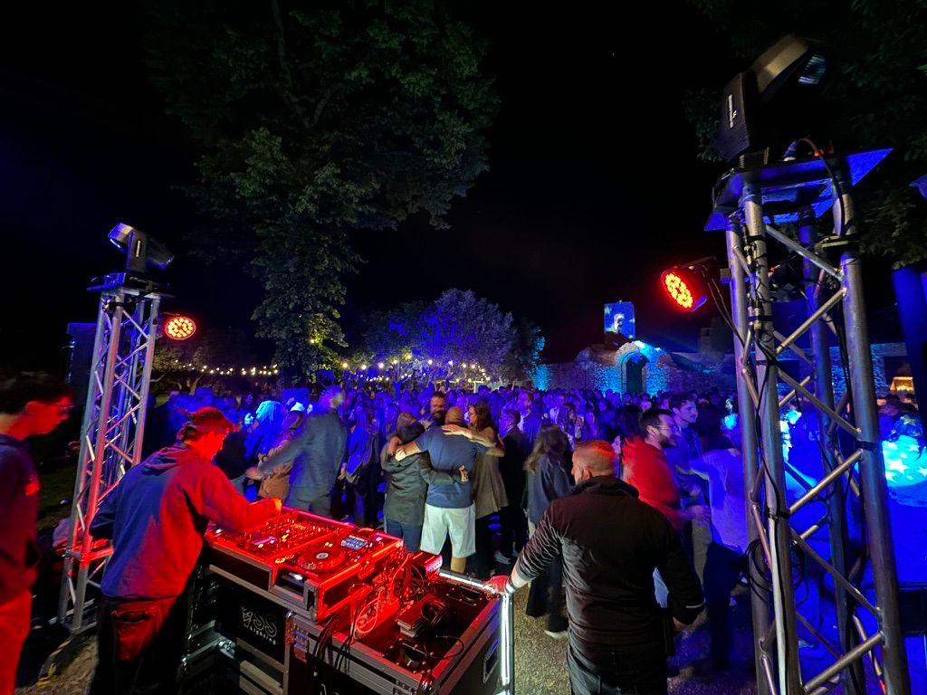 DJ booth between two truss towers with moving heads and washes, crowd behind