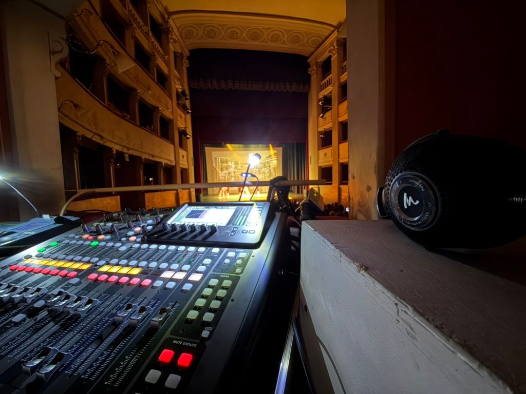 Mixer digitale in primo piano con il teatro all'italiana e il palco illuminato sullo sfondo