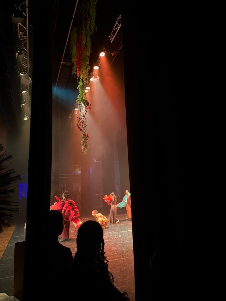 Palco visto da dietro le quinte, fascio di luce nel fumo e danzatori in costume